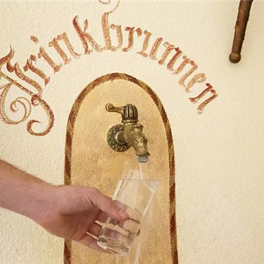 A drinking fountain with a faucet from which fresh water flows. A hand holds a glass to catch the water.