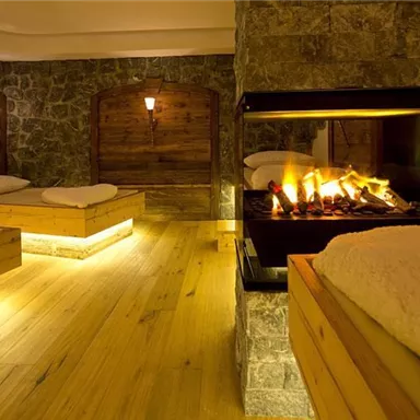 A relaxing wellness area with wooden loungers and gentle lighting. The fireplace creates a cozy atmosphere.
