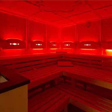 A quiet sauna room with red lights and wooden benches. The atmosphere is relaxing and inviting.