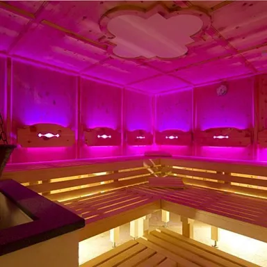 A modern sauna room with wooden benches and gentle, pink lighting. The room conveys a relaxing atmosphere.