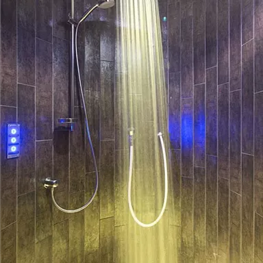 A modern shower with a gently falling water jet. The walls are lined with dark tiles and the lighting creates a relaxed atmosphere.