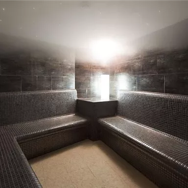 A modern steam bath area with seating made of mosaic tiles. Soft lighting creates a relaxing atmosphere.