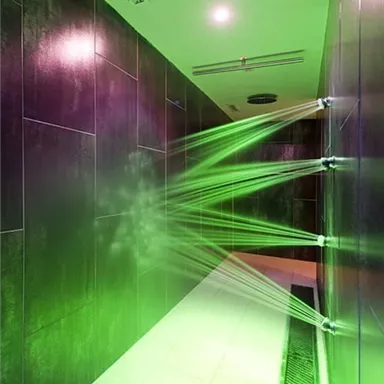 A modern shower area with green lighting and water jets. The walls are dark, and the atmosphere feels relaxing.