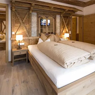 A cozy room with a wooden double bed and warm lighting. The walls are adorned with wooden panels, creating an inviting atmosphere.