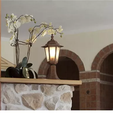 An elegant table lamp stands next to an orchid on a wooden shelf. In the background, arched openings are visible, creating a warm atmosphere.