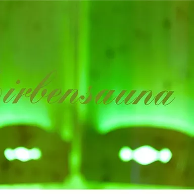 A relaxing larch sauna with gentle green lighting. The text "Zirbensauna" is prominently displayed in the foreground.