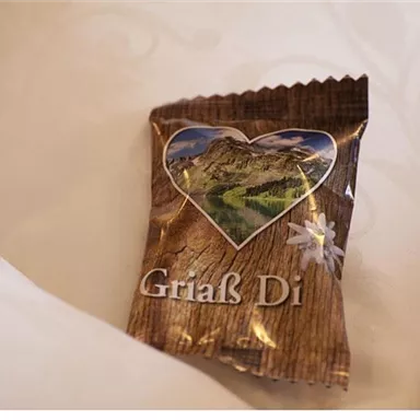 A small gift with the inscription "Griaß Di" in a heart design. The packaging features a mountain landscape and conveys a homely feeling.