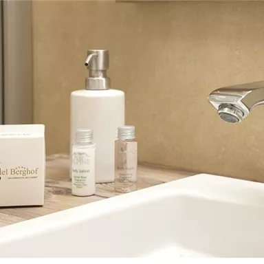 A modern bathroom with an elegant sink and shiny faucet. On the sink are small toiletries and a soap box.