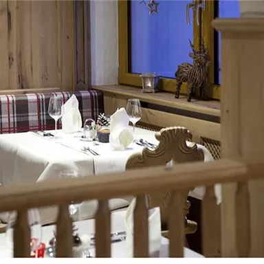 An elegant restaurant with a set table and cozy wooden paneling. The windows depict a wintry atmosphere with decorative elements.