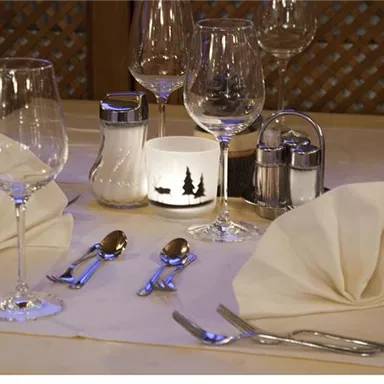 An elegantly set table with glasses, cutlery, and napkins. Soft candlelight creates a cozy atmosphere.