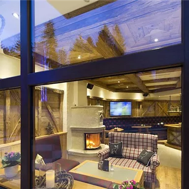 A cozy interior with a fireplace and modern furnishings. Large windows showcase a warm atmosphere with wooden details and pleasant lighting.