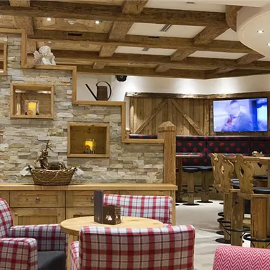A cozy interior with wooden details and a stone wall. Above the seating areas, there is appealing lighting and a television.