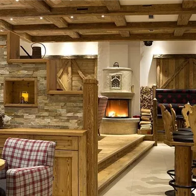 A cozy restaurant with rustic wood design and an open fireplace. The decor includes comfortable seating and decorative stone walls.