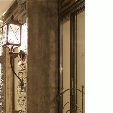 An elegant front door with a classic metal wall lamp. The stone wall adds a rustic charm to the ambiance.