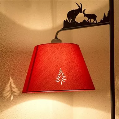 A red lamp with a stylized Christmas tree on the shade. The shadows of animals and trees are visible on the wall.