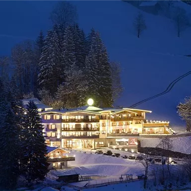 A cozy hotel in the mountains, surrounded by snow-covered trees. It is illuminated at night and conveys an inviting atmosphere.