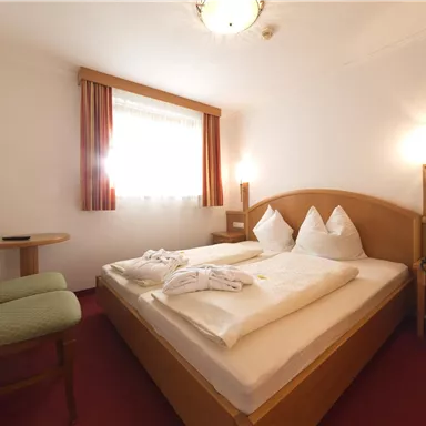 A cozy room with a double bed and two pillows. There is a table, a chair, and a television on the wall.