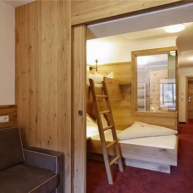 A cozy room with wooden paneling and a bunk bed. A sofa is next to the entrance, and the room feels bright and inviting.