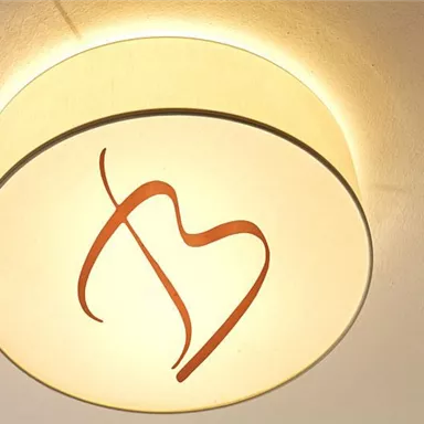 A round ceiling light with a soft, warm glow. At the center is a stylized, red symbol.