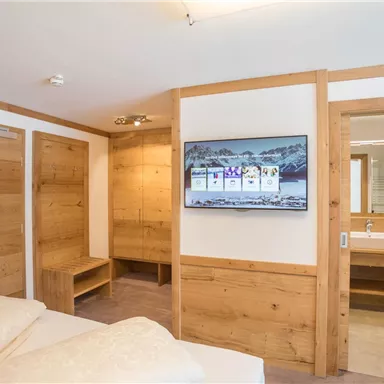 Ein modernes Zimmer mit Holzwänden und einem Flachbildfernseher. Es gibt ein bequemes Bett und ein angrenzendes Badezimmer mit Waschbecken.