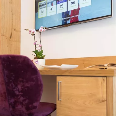 Ein moderner Arbeitsplatz mit einem Holzschreibtisch und einem lila Stuhl. Auf dem Bildschirm wird eine Willkommensnachricht angezeigt.