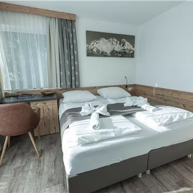 Ein gemütliches Zimmer mit einem Doppelbett und einer modernen Einrichtung. Das Licht fällt sanft durch die Fenster und schafft eine einladende Atmosphäre.