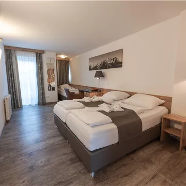 Ein helles Hotelzimmer mit zwei Betten und einem modernen Schreibtisch. Große Fenster lassen viel Tageslicht herein und es gibt eine gemütliche Stehlampe.