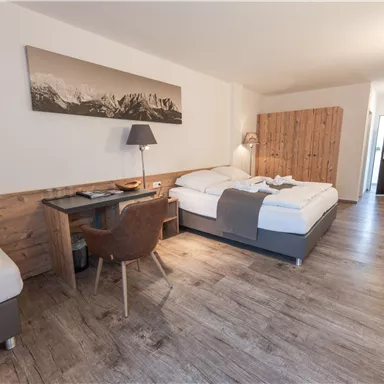 Ein modernes Hotelzimmer mit einem großen Doppelbett und einem kleinen Schlafbereich. Eine gemütliche Sitzecke mit Schreibtisch und Stuhl ist ebenfalls vorhanden.