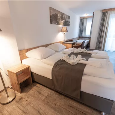 Ein modernes Hotelzimmer mit zwei Betten und stilvoller Einrichtung. Lichtdurchflutete Fenster sorgen für eine angenehme Atmosphäre.