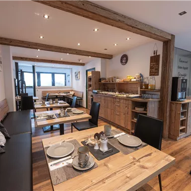 Ein einladendes Restaurant mit Holzinterieur und gemütlichen Tischen. Der Raum ist hell und bietet einen Frühstücksbuffet-Bereich.