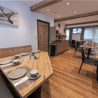 Ein gemütliches Restaurant mit Holztischen und Stühlen. Die Wände sind hell gestrichen und mit Fotos dekoriert.