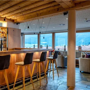 A modern café with a wooden bar and cozy seating. Large windows offer a view of the surrounding landscape.