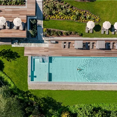 A beautiful outdoor pool with loungers and umbrellas in a well-maintained garden landscape. The scene looks relaxed and inviting.