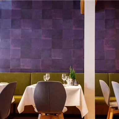 A stylish restaurant with round tables and elegant chairs. The walls are decorated in a patterned shade of purple.
