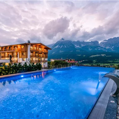 A modern building with a beautiful pool, surrounded by a picturesque mountain landscape. The sky is cloudy, giving the scene a tranquil atmosphere.