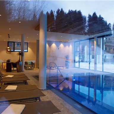 A modern spa facility with an indoor pool and loungers. Large windows offer a view of a snowy landscape.