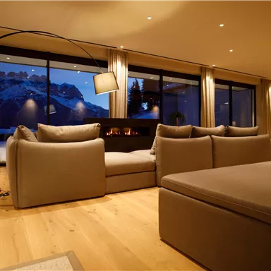 A modern living room with a cozy sofa and a large window that offers a view of snow-covered mountains. The lighting is warm and inviting.