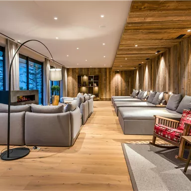 A modern living room with large windows and cozy seating. The wooden floor and wall paneling create a warm, inviting atmosphere.