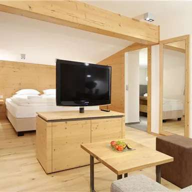A modern room with wooden walls and a large TV. There is a bed, a coffee table, and a cozy seating area.