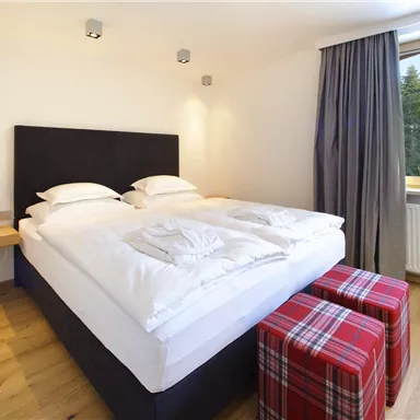 A cozy bedroom with a large bed and bright bedcovers. The windows offer a view of nature, while a stylish lamp provides pleasant lighting.