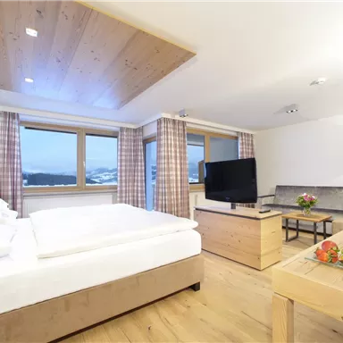 A modern room with wood decor, large windows, and a television. Fresh fruits and flowers are arranged on the table.