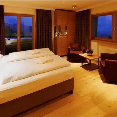 A cozy hotel room with a double bed and wooden interior. The large windows offer a view of the surroundings.