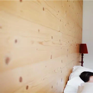 A sleeping person in a cozy bed. In the background, there is a wooden wall and a red lamp visible.
