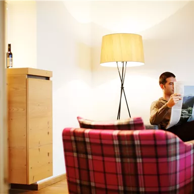 A cozy living situation with a man reading a newspaper. In the background, there is a modern floor lamp and a wooden wardrobe.