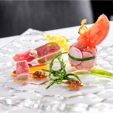 An elegant dish with fresh fish, vegetables, and fine sauces on a transparent plate. The presentation is creative and appealing.