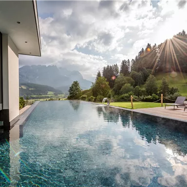 A stylish swimming pool with a view of the mountains and beautiful scenery. The sun shines through the clouds and reflects in the water.