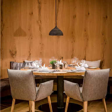 An elegant dining area with a round table and upholstered chairs. The walls are made of wood, creating a cozy atmosphere.