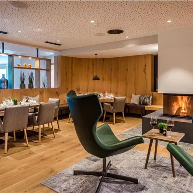 A modern restaurant with wooden paneling and elegant furniture. The fireplace creates a cozy atmosphere.