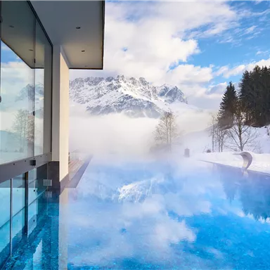 A modern building with an infinity pool in the mountains. The surroundings are snow-covered and the landscape is majestic.