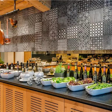 A stylish kitchen with a variety of fresh ingredients and beautiful wall decoration. On the counter, different bottles and bowls with vegetables and herbs are arranged.